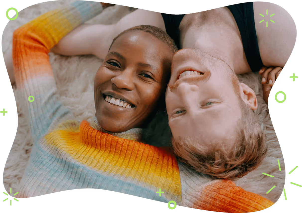Two people lying with their heads together on the floor smiling at the camera.